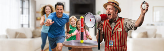 A carnival barker announces through a megaphone as a smiling family races toward an Element fire extinguisher displayed on a table.