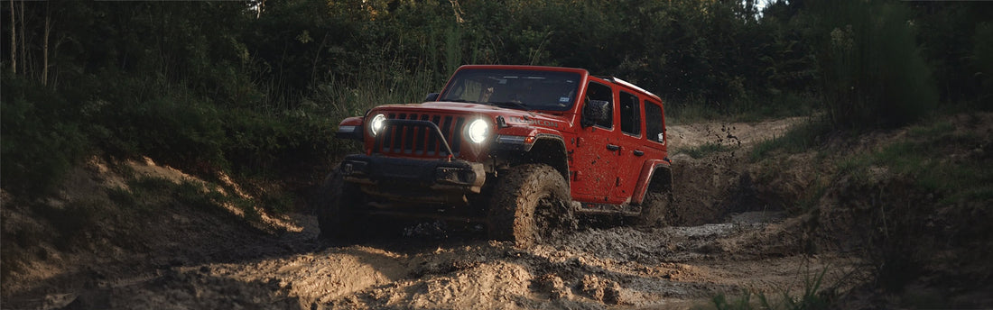 A Jeep Wrangler pulling through a muddy dip. 