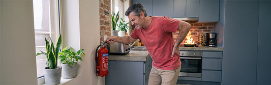 a middle aged man with a bad back trying to lift a heavy extinguisher.